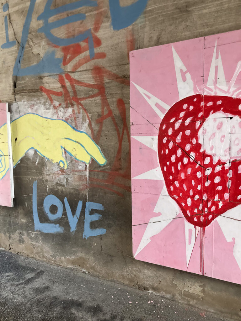 Katutaidetta Tarton kaduilta. Kuvassa keltainen käsi tiputtaa sanan "Love". Vieressä suuri mansikka vaaleanpuna-valkoisella pohjalla.